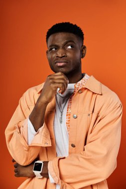 Genç Afro-Amerikalı adam elleri çenesinde turuncu ceketli poz veriyor..