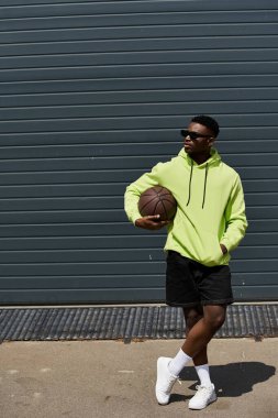 Neon yeşil kapüşonlu Afrikalı Amerikalı adam basketbol oynuyor..