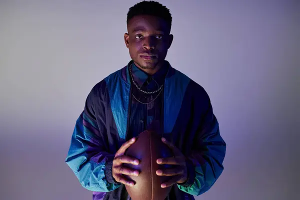 stock image Handsome African American man holding a football, against a vibrant blue backdrop.