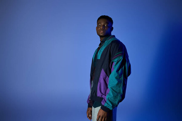 African American man wearing colorful jacket, standing against blue backdrop.