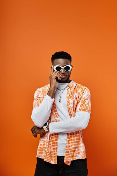 Красивый афроамериканец в солнечных очках и оранжевой рубашке на оранжевом фоне.