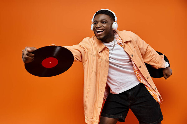 Черный мужчина в наушниках держит пластинку на оранжевом фоне.