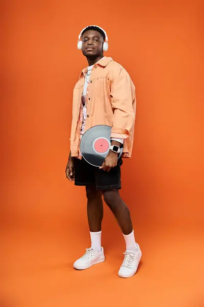 stock image Stylish man with headphones holding a record on orange background.