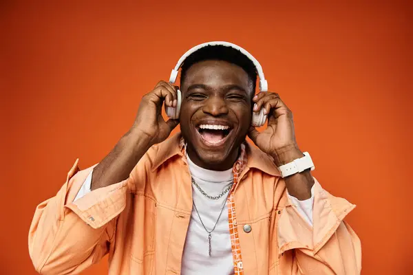 stock image Stylish black man listening to music with headphones on bright orange background.