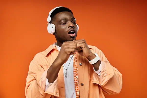 stock image A fashionable young African American man wearing headphones against an orange background.