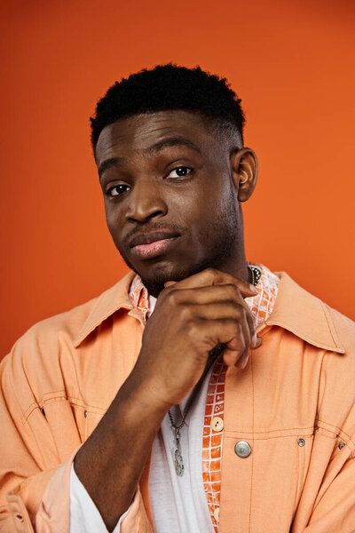 Стильный молодой человек уверенно позирует в яркой оранжевой куртке.