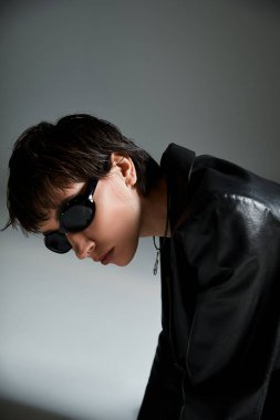 Stylish woman leaning against a wall wearing black sunglasses.