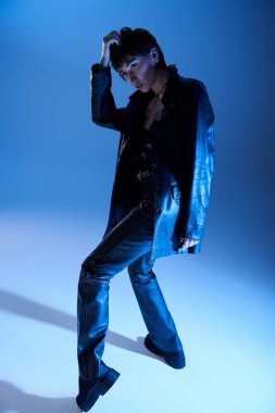 A fashion-forward woman striking a pose in front of a vibrant blue backdrop.