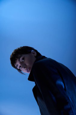 Stylish woman in black jacket poses gracefully against vibrant blue backdrop.