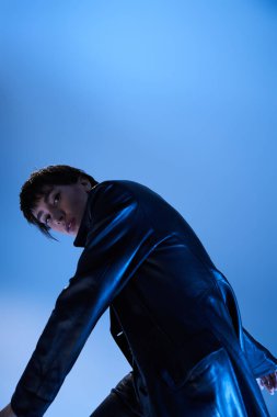 A woman in a leather jacket stands on a blue background.