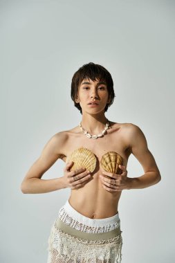 A beautiful woman in stylish attire gently cradling a shell on her chest.