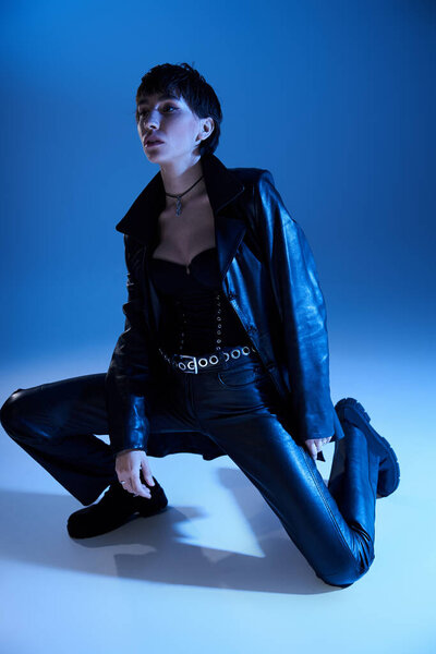 Stylish woman in black leather pants crouching on floor.