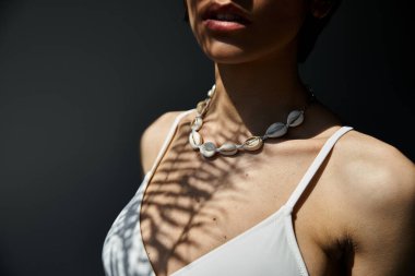 A woman adorned in a stylish seashell necklace poses gracefully.