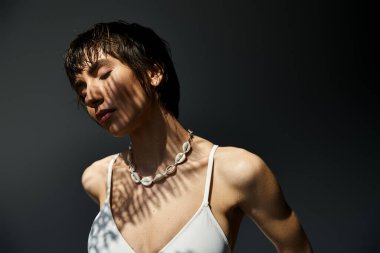 A stylish young woman poses in a white bikini against a dark background.