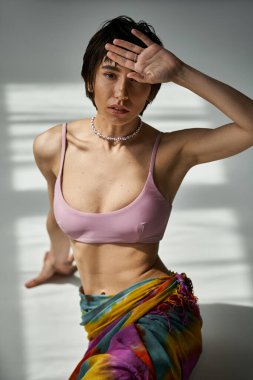 Young woman in pink bikini striking a pose with hand on face.