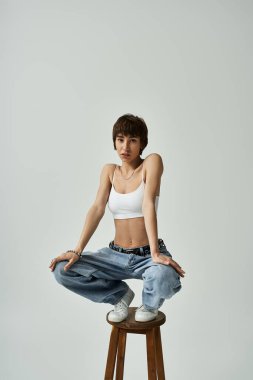 A stylish, active young woman poses on a stool.