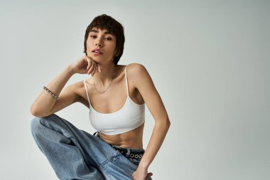 A young woman in jeans and a white top striking a pose on a white background.