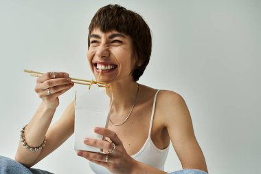 Young woman enjoying noodles with chopsticks on white background.