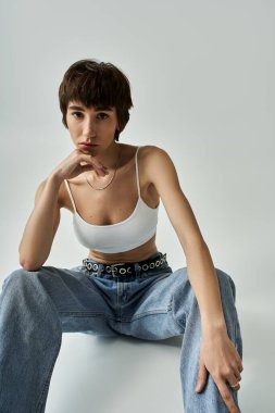Stylish woman in white top and jeans sitting gracefully on floor.