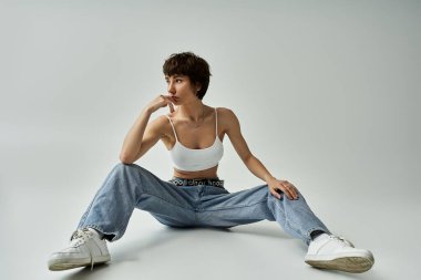Stylish young woman sitting gracefully in white attire on a minimalist background.