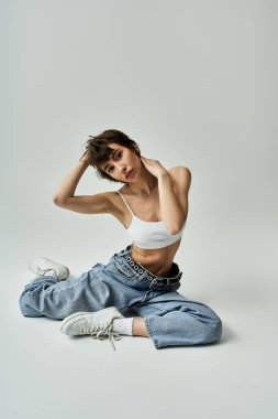Stylish young woman in white tank top and jeans striking a dynamic pose on a white background.