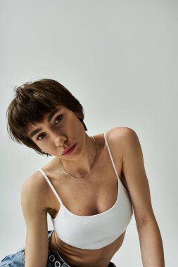 Stylish young woman posing in a white bra top on white backdrop.