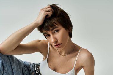 Stylish young woman posing confidently in white tank top and jeans.