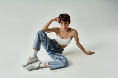 Stylish woman in white top and jeans sitting gracefully on floor.