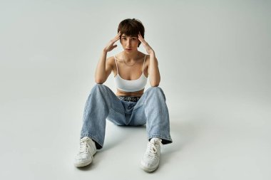 Stylish woman sitting on floor with hands on head.