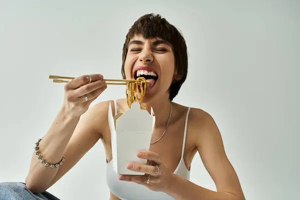 stock image Stylish woman in a chic outfit gracefully eating noodles using chopsticks.