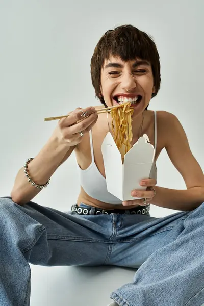 stock image Woman in stylish attire savors noodles while sitting gracefully on the floor.