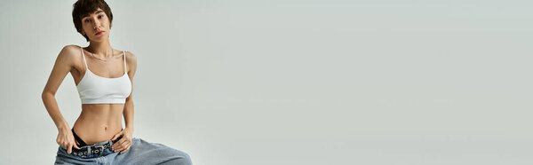 A stylish young woman in a white tank top and jeans strikes a captivating pose.