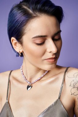 A pretty young woman with short blue hair poses elegantly in a silver party dress adorned with a necklace.
