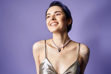 A stylish young woman with short blue hair striking a pose in a shimmering silver party dress and a necklace.
