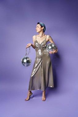A young woman with short blue hair poses in a stunning silver dress while holding two sparkling silver balls.