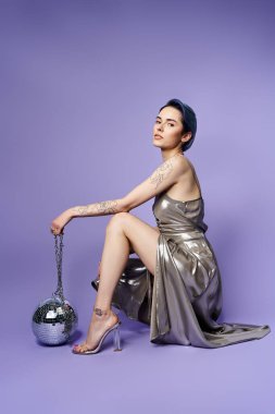 A young woman with short blue hair posing elegantly in a silver party dress