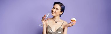 A young woman with short blue hair, dressed in a silver party dress, holding a cupcake and a glass of wine.
