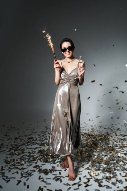 A charming young woman with short blue hair poses in a silver party dress, holding a sparkling wand.
