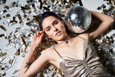 A young woman with blue hair dazzles in a silver dress while elegantly holding a disco ball.
