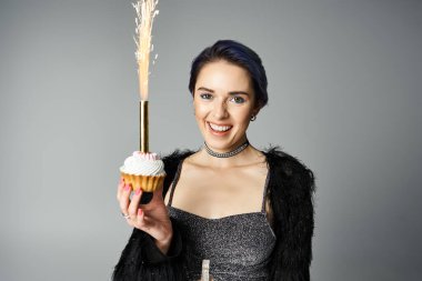 A stylish young woman with short dyed hair holding a cupcake topped with a delicate feather. clipart