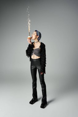 Edgy young woman with dyed hair and stylish clothes licking cupcake