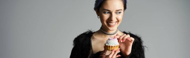 Stylish birthday girl with dyed hair holds a scrumptious cupcake in her hands. clipart