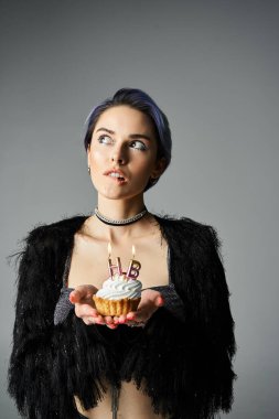 Young woman holding cupcake with lit candle in stylish setting, celebrating a birthday.