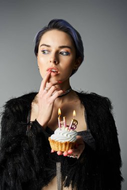 A young woman in stylish attire holds a cupcake with lit candles, a birthday girl ready to make a wish. clipart