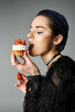 A fashionable young woman with short dyed hair enjoys a cupcake topped with strawberries in a studio setting. clipart