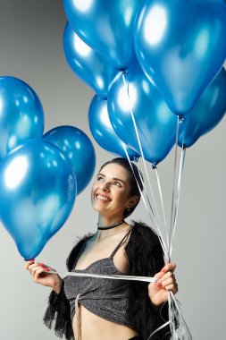 A young woman with colorful hair holding a bundle of blue balloons in a stylish studio.