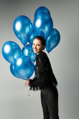 A stylish young woman with short dyed hair holding a bunch of bright blue balloons in a studio setting.