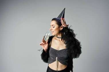 A young woman with short dyed hair dons a party hat while elegantly holding a glass of champagne