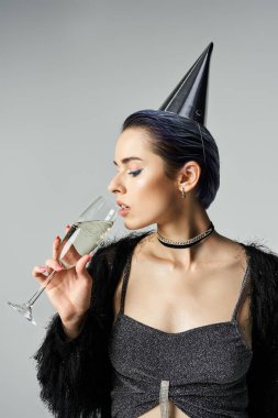 A stylish young woman with short dyed hair, wearing a party hat, holding a champagne glass.