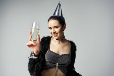 Young woman in fashionable outfit and party hat holds champagne glass for birthday celebration.